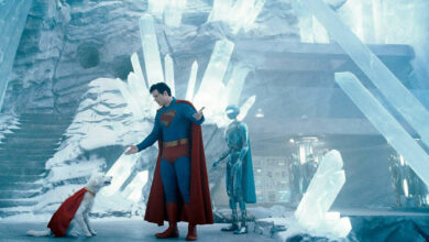 A imagem mostra um personagem vestido como super-herói, com um traje azul e uma capa vermelha, interagindo com um cachorro que também usa uma capa vermelha. Ao fundo, há uma estrutura de cristais de gelo e um robô prateado. O ambiente é gelado e iluminado, com uma atmosfera futurista.