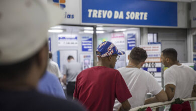 A imagem mostra uma fila de pessoas em uma lotérica chamada